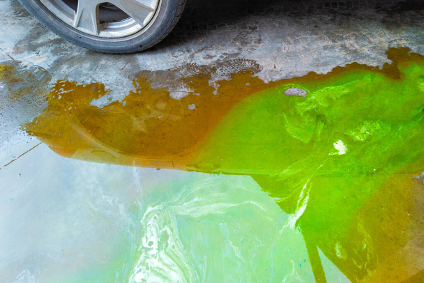 車の近くのコンクリートの床の緑のクーラントそして茶色の技術的な液体のプリドル. - 写真・画像