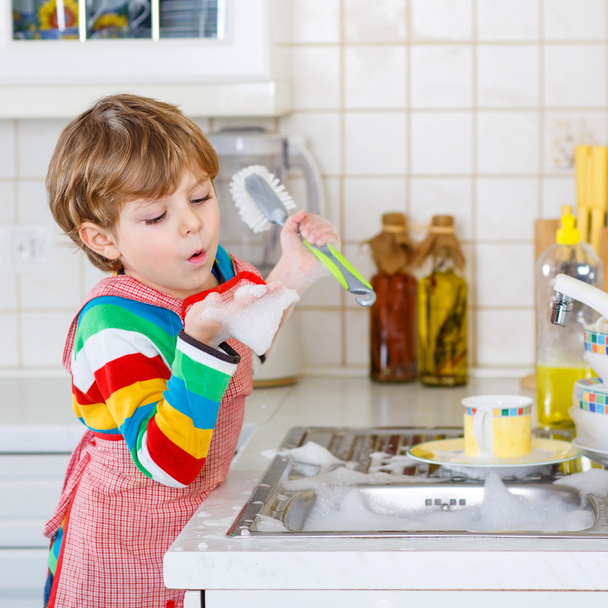 Adorable toddler child washing dishes in domestic kitchen.  - Photo, Image