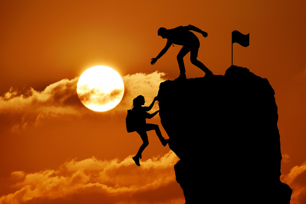 二人の男と女の方の共同作業のチームワークは、登山隊、美しい日没の風景の上にお互いを助ける. - 写真・画像