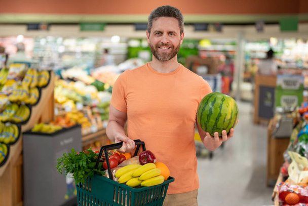 Portrait of hispanic man with shopping basket purchasing food in grocery store. Sales and shopping. Man buying products at supermarket. Supermarket and grocery shop. Discount, sale concept - Foto, afbeelding