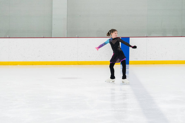 Young girl perfecting her figure skating routine while wearing her competition dress at an indoor ice rink. - Photo, Image