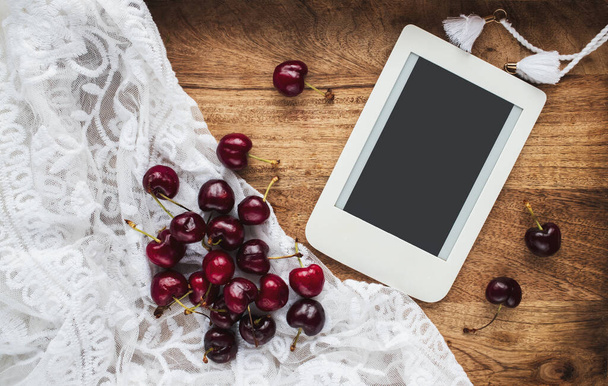 Composición con cerezas dulces en un encaje y e-reader con espacio para copiar. Plantilla para blog femenino redes sociales. - Foto, imagen
