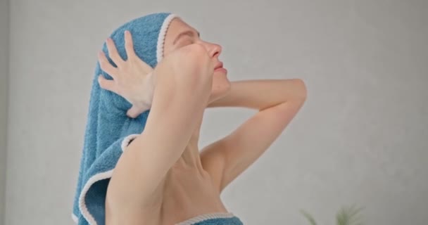 Belle jeune femme enveloppant les cheveux dans une serviette en coton bleu après la douche, en mouvement. Vue latérale de la femme heureuse et détendue mettant une serviette sur la tête humide, essuyant dans la salle de bain. Concept de routine de soins capillaires. - Séquence, vidéo
