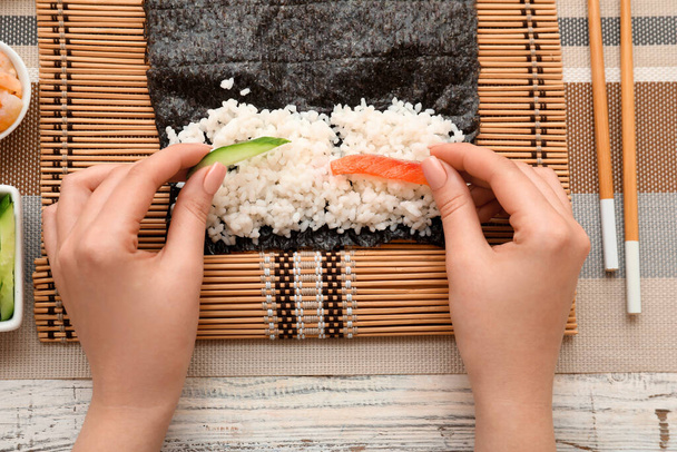 Frau bereitet Sushi-Rollen auf hellem Holzgrund zu, Nahaufnahme - Foto, Bild