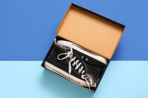 Boîte en carton avec des chaussures décontractées élégantes sur fond bleu - Photo, image