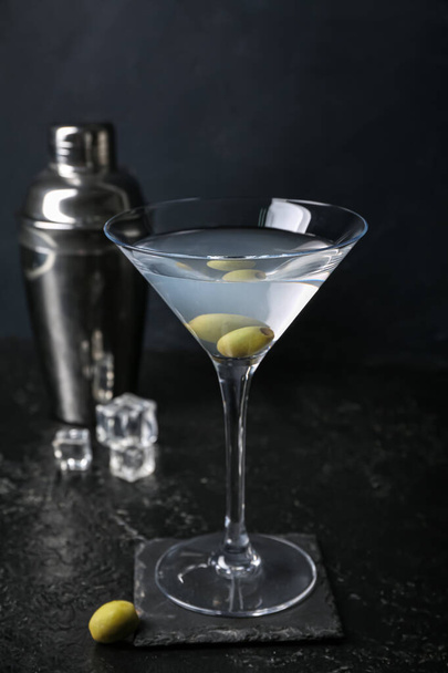 Verre de martini savoureux aux olives et shaker sur fond sombre - Photo, image