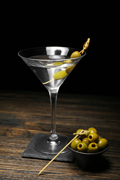 Стакан вкусного мартини и зеленых оливок на тёмном деревянном столе - Фото, изображение