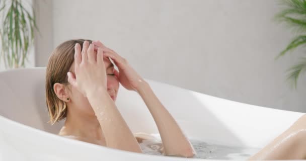 Relaxed beautiful woman taking salt bath at home. Side view of pretty blonde female with closed eyes soaking in modern bathtub at luxury resort, in slow motion. Concept of self care, recreation, spa.  - Footage, Video