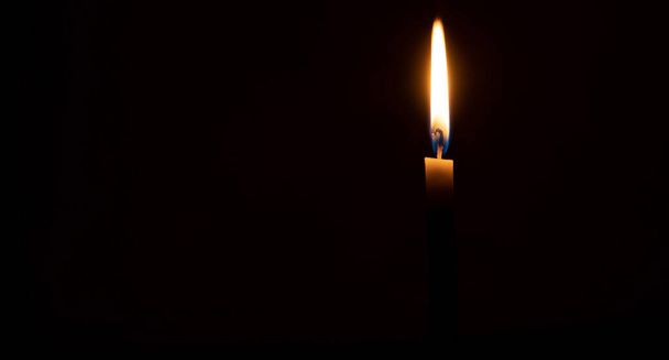 Una sola llama o luz de vela encendida brilla sobre una vela naranja sobre fondo negro u oscuro en la mesa de la iglesia para Navidad, funeral o servicio conmemorativo con espacio para copias - Foto, imagen