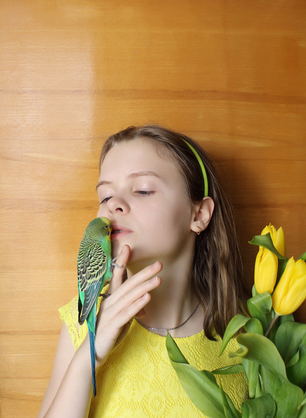 Young girl with green bird (little parrot) and yellow flowers - Photo, Image