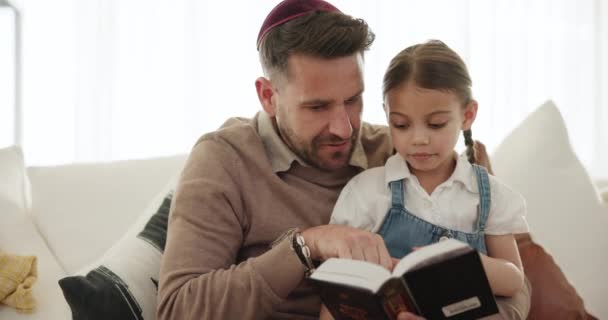 Religion, reading and father with book and girl in home, teaching and learning about Torah and spiritual knowledge. Child, education and sharing Jewish gospel, faith or history of culture on sofa. - Footage, Video