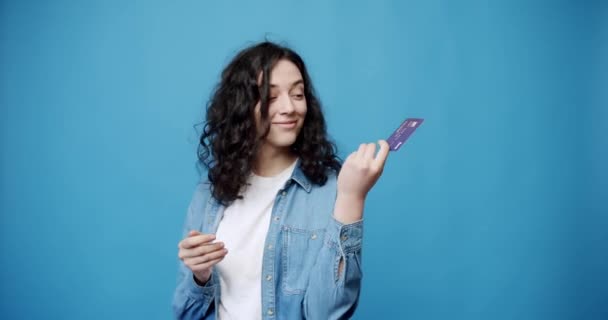 Easy banking, money and payment concept. Smiling woman hold bank card in hand and showing thumb-up gesture on blue background. Female recommend using credit card for online purchase - Footage, Video