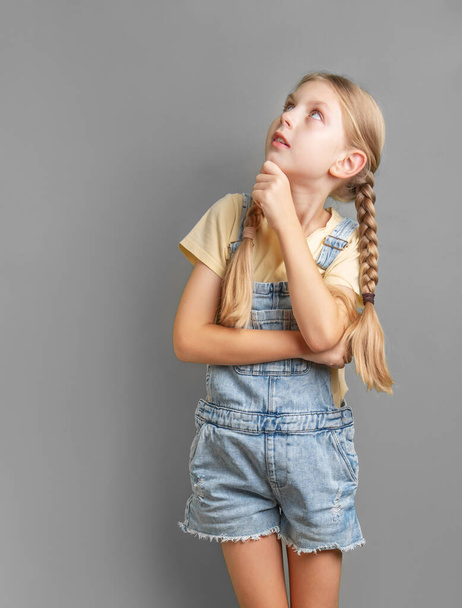 Porträt eines kleinen Mädchens mit geflochtenem Haar, das nachdenkt und aufblickt - Foto, Bild