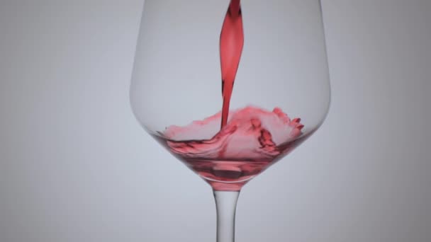 Wein im Weinglas auf weißem Hintergrund. Nahaufnahme. Zeitlupe beim Einschenken von Rotwein. - Filmmaterial, Video