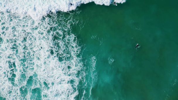 空中からの眺め波がサーフボードの上に横たわっているのを待っている未知のサーファー。極端なサーファーはターコイズブルーの海のスローモーションでスケートボードを楽しむ。熱帯のビーチで飛び散る泡嵐の水.  - 写真・画像