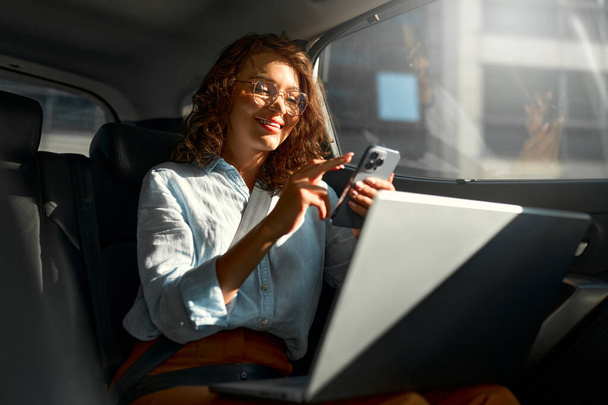 Vonzó üzleti nő dolgozik rajta laptop egy autó hátsó Sit, és útban a találkozó arufeltolto. - Fotó, kép