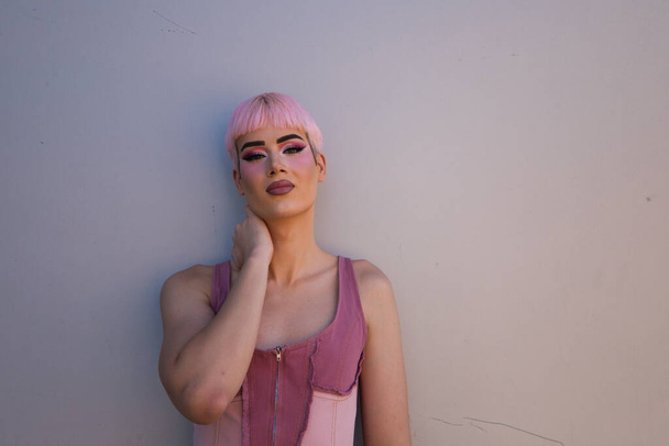 Portret młodego geja z różowymi włosami i makijażem stojącego na białym tle i robiącego różne miny twarzą i rękami. Pojęcie równości i praw LGBTQ - Zdjęcie, obraz