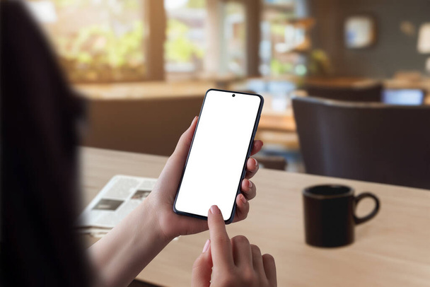 Morgen koffie scene. Vrouw met smartphone met geïsoleerd scherm voor app-presentatie, vergezeld van een krant op tafel. Perfect voor het presenteren van technologie en leesgewoonten - Foto, afbeelding