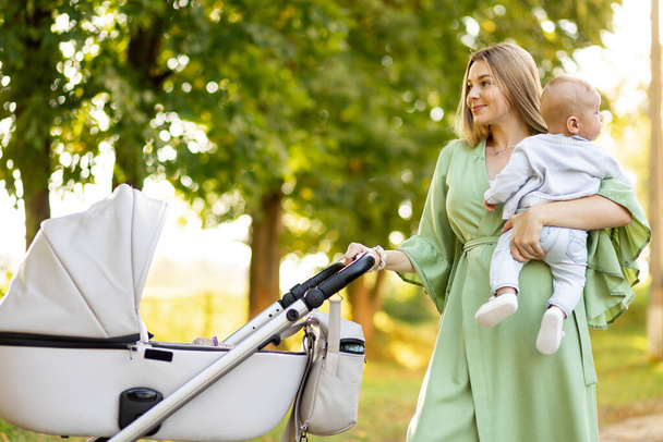family, child and parenthood concept - happy mother with stroller in park - Photo, Image