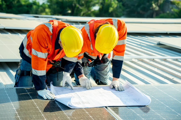 Profesjonalni inżynierowie sprawdzają dach słoneczny na dachu fabryki w świetle słonecznym. Inżynierowie wykonujący prace serwisowe w zakresie energii elektrycznej odnawialnej - Zdjęcie, obraz