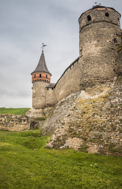 La parte del Vecchio Castello Kamianets-Podilskyi sotto un cielo nuvoloso. Potenti bastioni e torri della fortezza situata tra la pittoresca natura nella città storica di Kamianets-Podilskyi, - Foto, immagini
