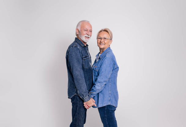 Вид сбоку любящих зрелых мужа и жену, держащихся за руки и улыбающихся камере на белом фоне - Фото, изображение