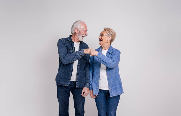 Vrolijke senior man en vrouw geven vuist hobbels en kijken naar elkaar op witte achtergrond - Foto, afbeelding
