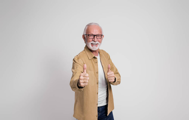 Succesvolle senior zakenman glimlachend en met duimen omhoog gebaar over geïsoleerde witte achtergrond - Foto, afbeelding