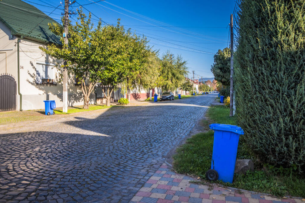 Blauwe vuilnisbakken op straat in een klein stadje in de buurt van elk huis. Gecentraliseerde afvalverzameling in een kleine gezellige Europese stad. Afvalverzameling op een bepaalde dag van de week. - Foto, afbeelding