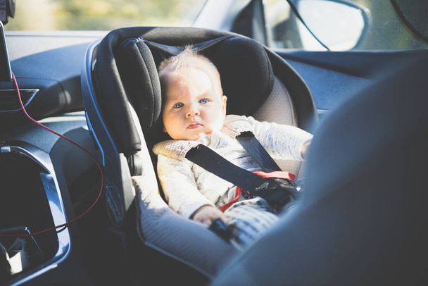 Симпатичний маленький хлопчик прив'язаний до дитячого автокрісла в пасажирському салоні під час водіння автомобіля
 - Фото, зображення
