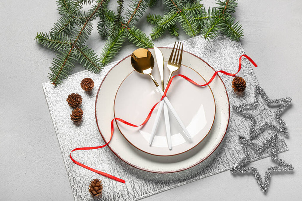 Накрытие рождественского стола с елочными ветвями, шишками и золотыми столовыми приборами на сером фоне - Фото, изображение