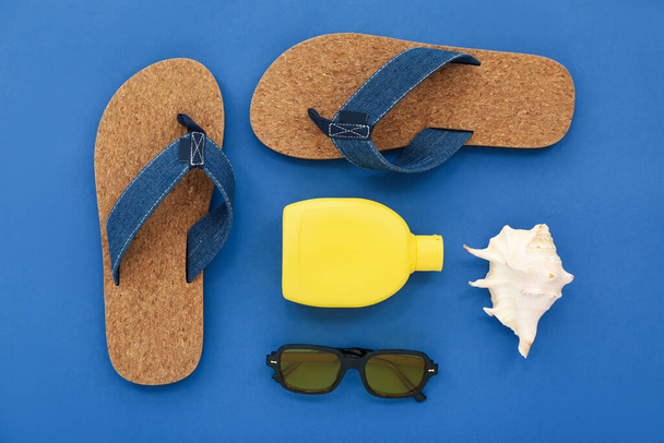 Ζεύγος σανδάλια με αντηλιακή κρέμα και γυαλιά ηλίου σε μπλε φόντο - Φωτογραφία, εικόνα