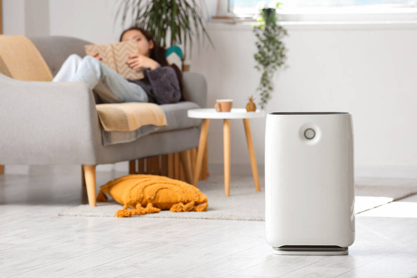 Air purifier against blurred woman reading book on sofa in living room - Photo, Image