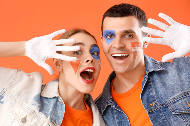 Junges Paar mit geschminkten Gesichtern auf orangefarbenem Hintergrund, Nahaufnahme - Foto, Bild