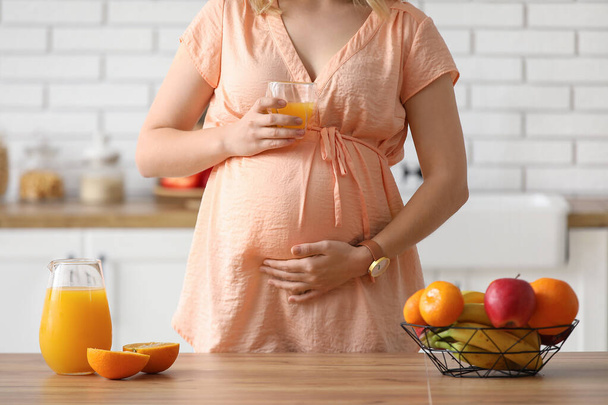 Jeune femme enceinte avec un verre de jus à table dans la cuisine - Photo, image