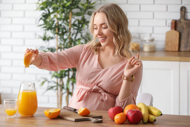 Young pregnant woman with orange and juice at table in kitchen - Photo, Image