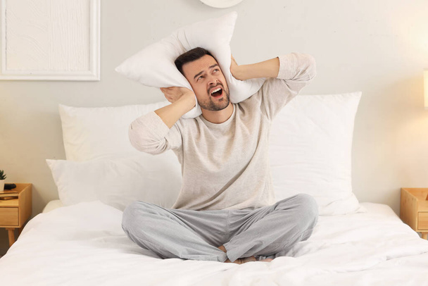 Joven con almohada sufriendo de vecinos ruidosos en el dormitorio - Foto, Imagen