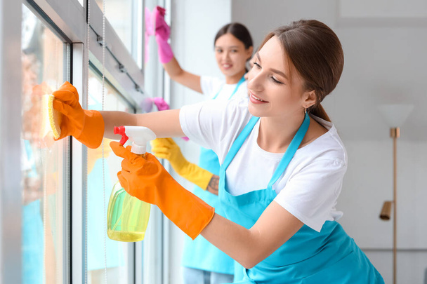 Conserje hembra limpiando ventana en la habitación
 - Foto, imagen