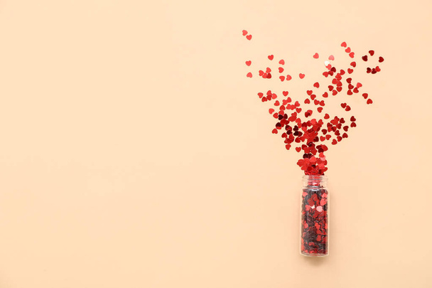 Botella con lentejuelas en forma de corazón sobre fondo de color. Celebración de San Valentín - Foto, imagen