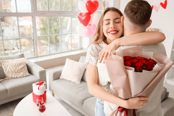 Beautiful young happy couple with bouquet of roses celebrating Valentine's Day at home - Photo, Image