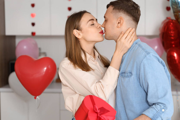 Gyönyörű fiatal pár ajándék doboz ünnepli Valentin-nap csók a konyhában otthon - Fotó, kép