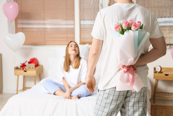 Junger Mann begrüßt seine Freundin zu Hause mit einem Strauß Tulpen zum Valentinstag - Foto, Bild