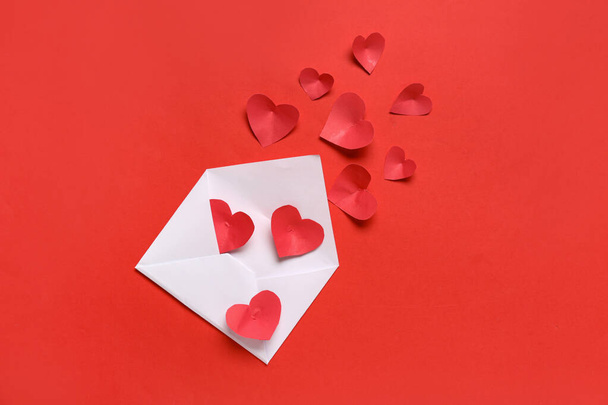Samenstelling met enveloppe en papieren hartjes op rode achtergrond. Valentijnsdag - Foto, afbeelding