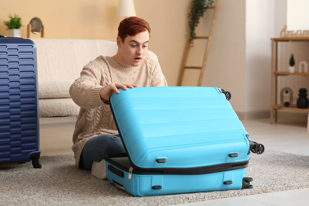 Surprised young man with open suitcase at home - Foto, afbeelding