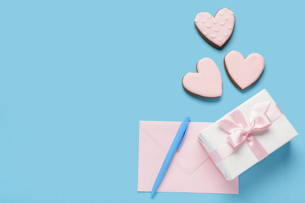 Herzförmige süße Kekse mit Geschenkverpackung und Umschlag auf blauem Hintergrund. Valentinstag-Feier - Foto, Bild