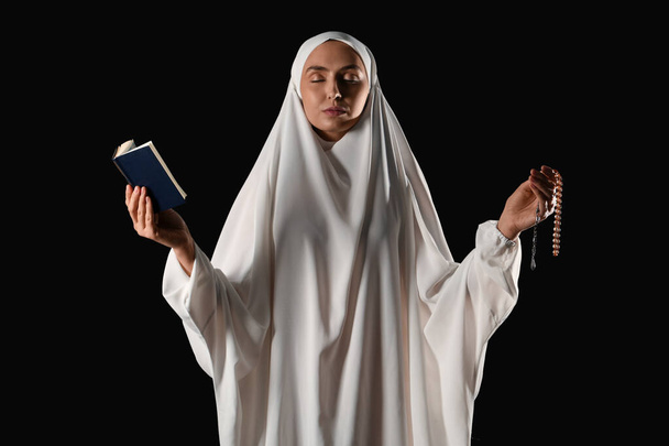 Joven musulmana con Corán y cuentas rezando sobre fondo negro - Foto, imagen