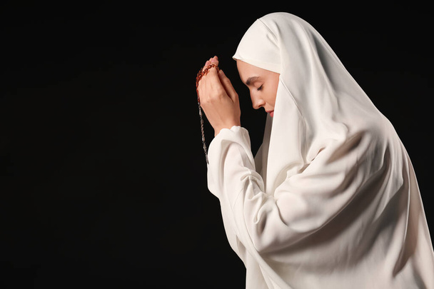 Young Muslim woman with beads praying on black background - Photo, Image