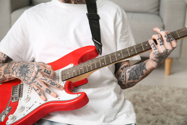Fresco tatuato giovane uomo che suona la chitarra elettrica a casa - Foto, immagini