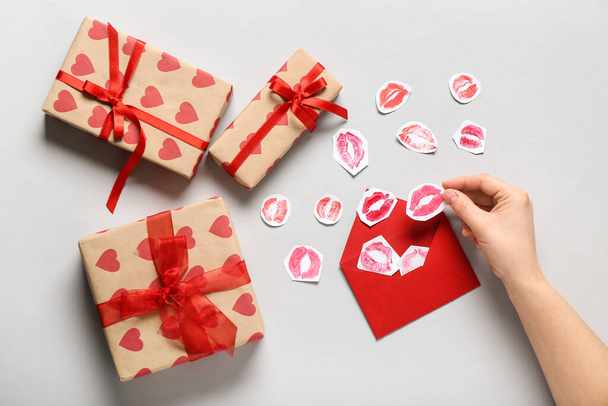 Female hand with lipstick kiss marks, envelope and gifts for Valentine's Day celebration on grey background - Photo, Image