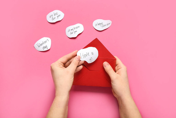 Manos femeninas con sobre rojo y declaraciones de amor sobre fondo rosa, primer plano. Celebración de San Valentín - Foto, imagen